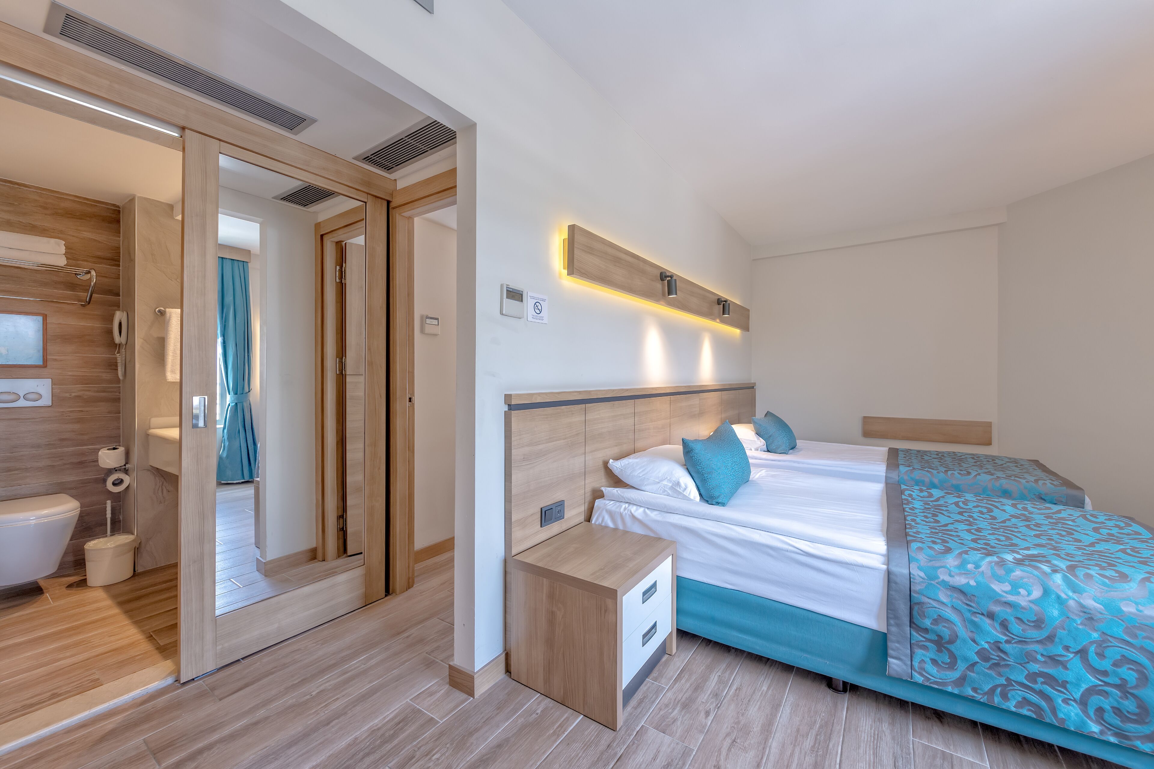 Una habitación de hotel moderna con suelo de madera, una cama con colcha azul estampada, una mesita de noche y un espejo.