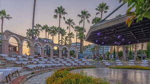An outdoor seating area with tables and chairs, palm trees, and a stone pathway. - Meryan Hotel - All Inclusive (Alanya)