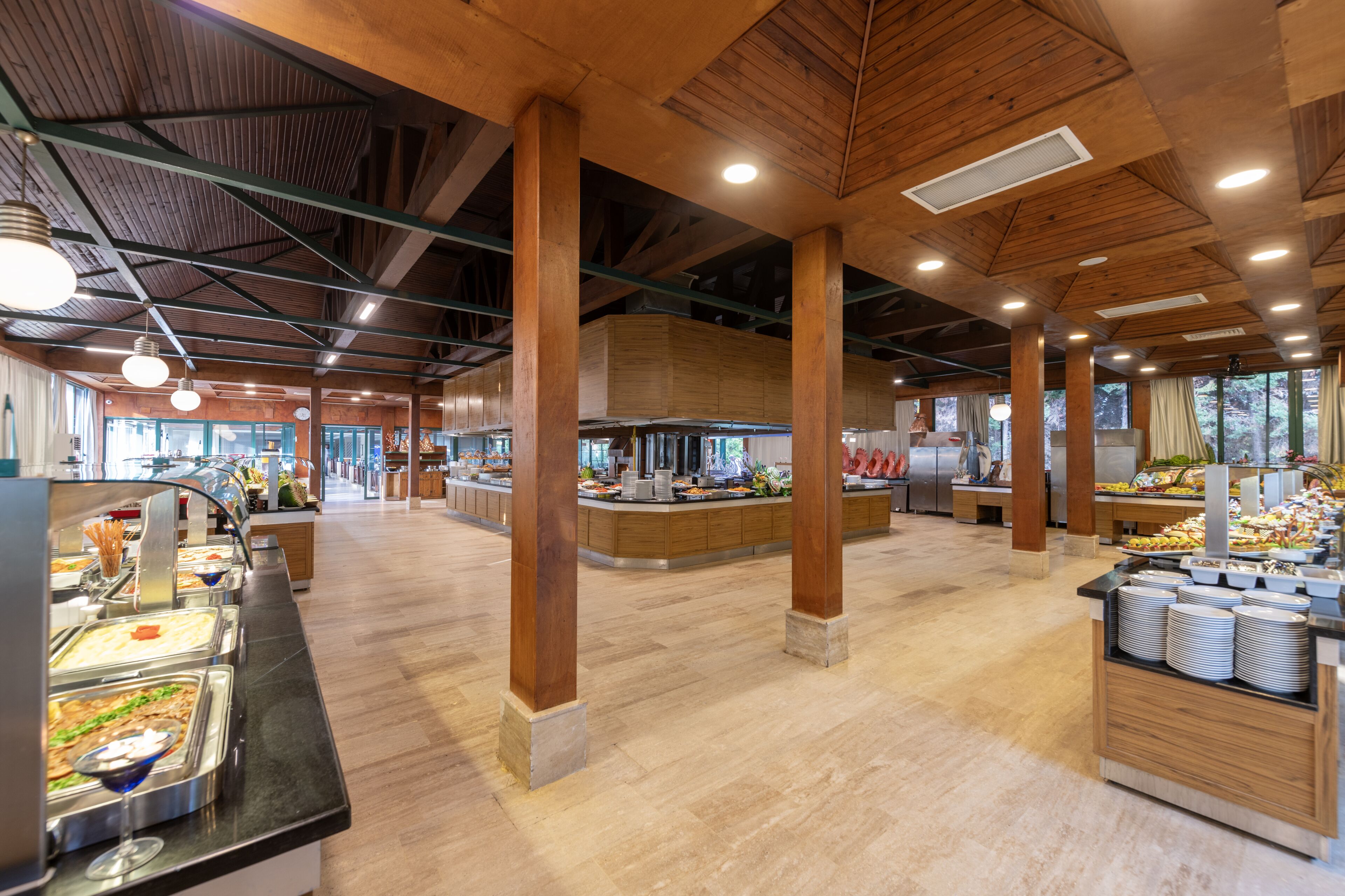 A spacious buffet area with multiple food stations, wooden beams, and a high ceiling.