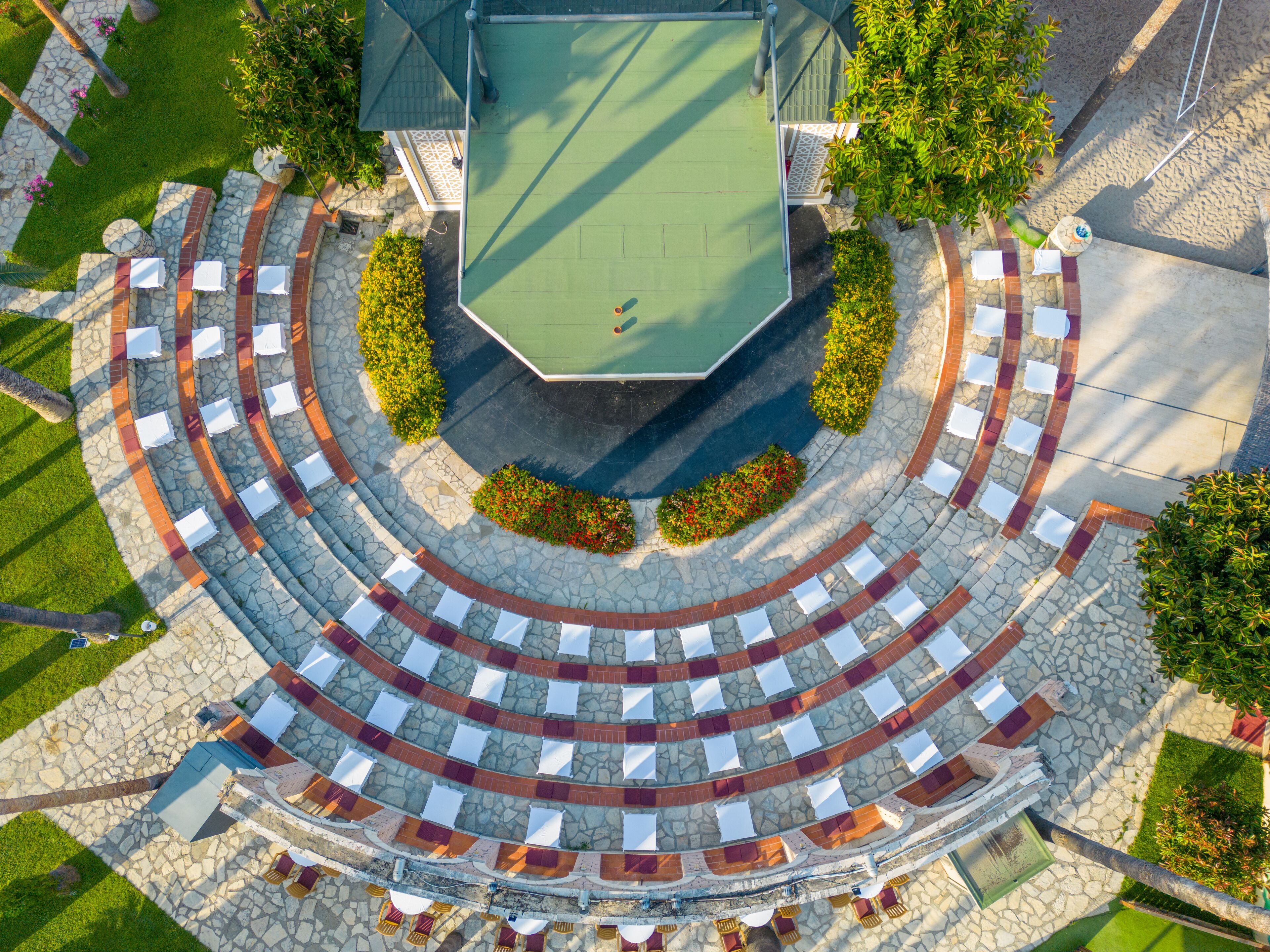 An outdoor amphitheater with tiered seating, a central stage, and surrounding greenery.