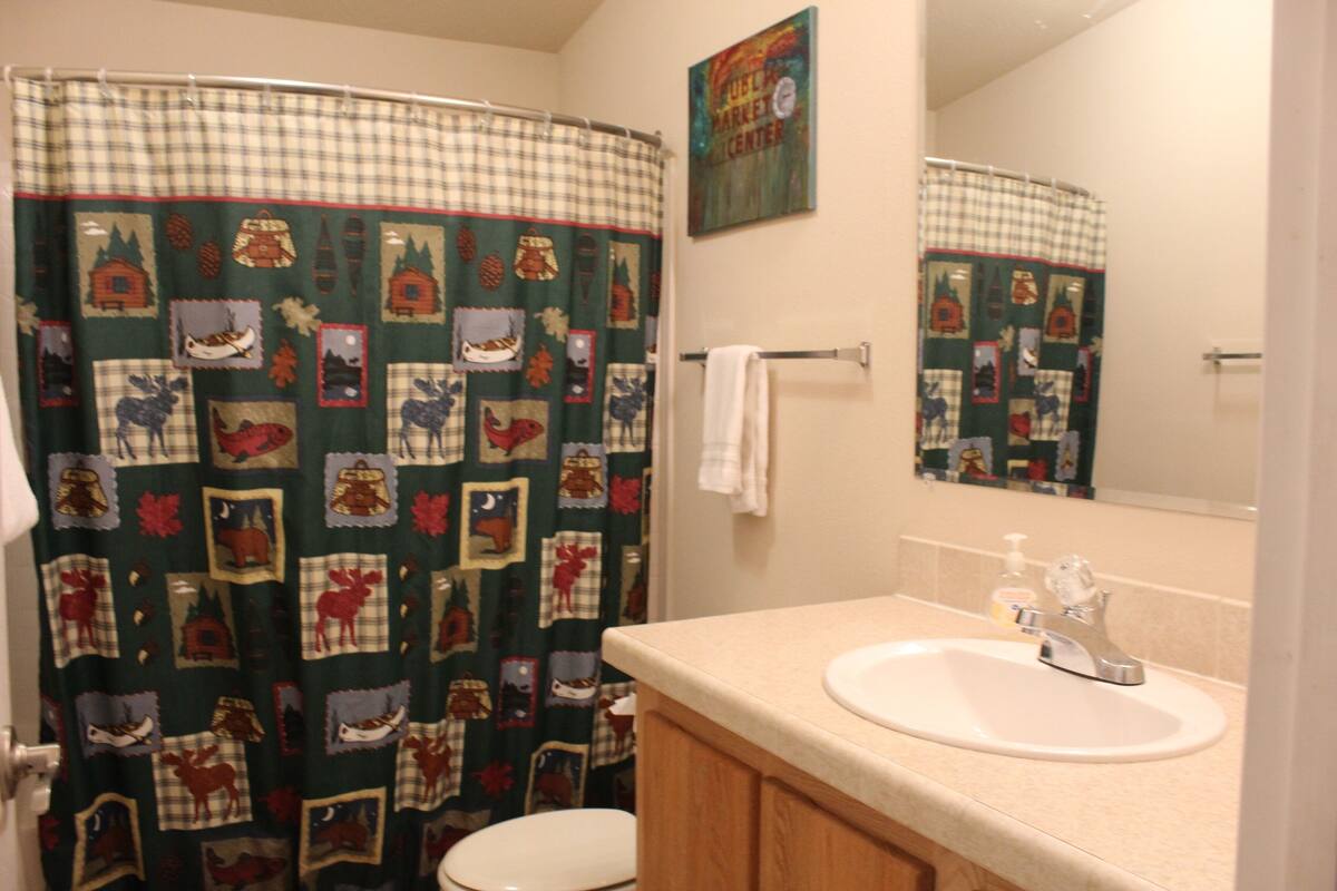 A bathroom with a checkered shower curtain, a toilet, a sink with a mirror, and a towel rack.