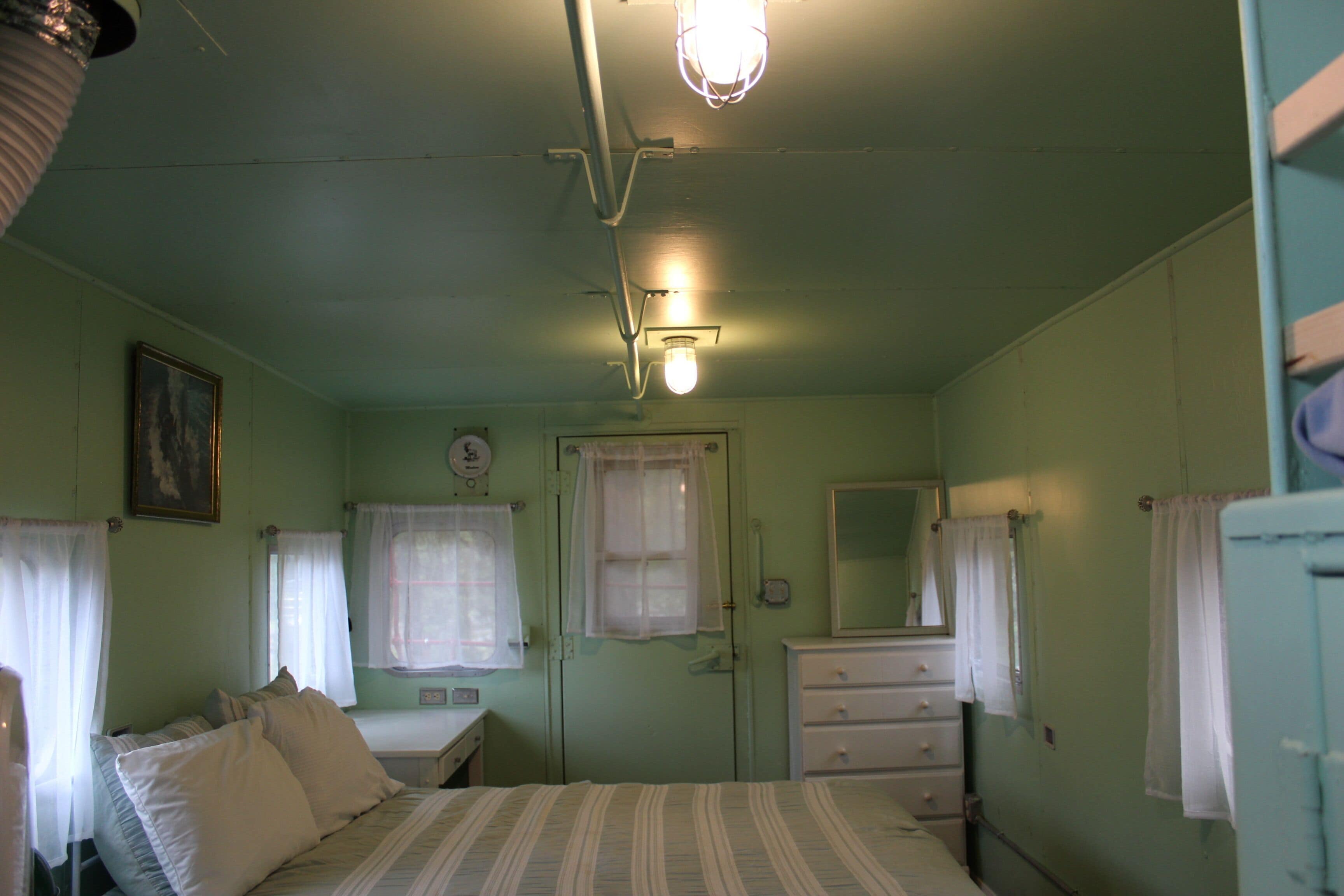 A room with a bed, a dresser, a mirror, and a window with curtains.
