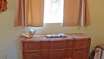 A room with a wooden dresser, a window with curtains, a patterned rug, and a small basket on the dresser.