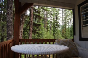 Une terrasse en bois avec une table ronde et un banc rembourré, donnant sur une forêt dense.