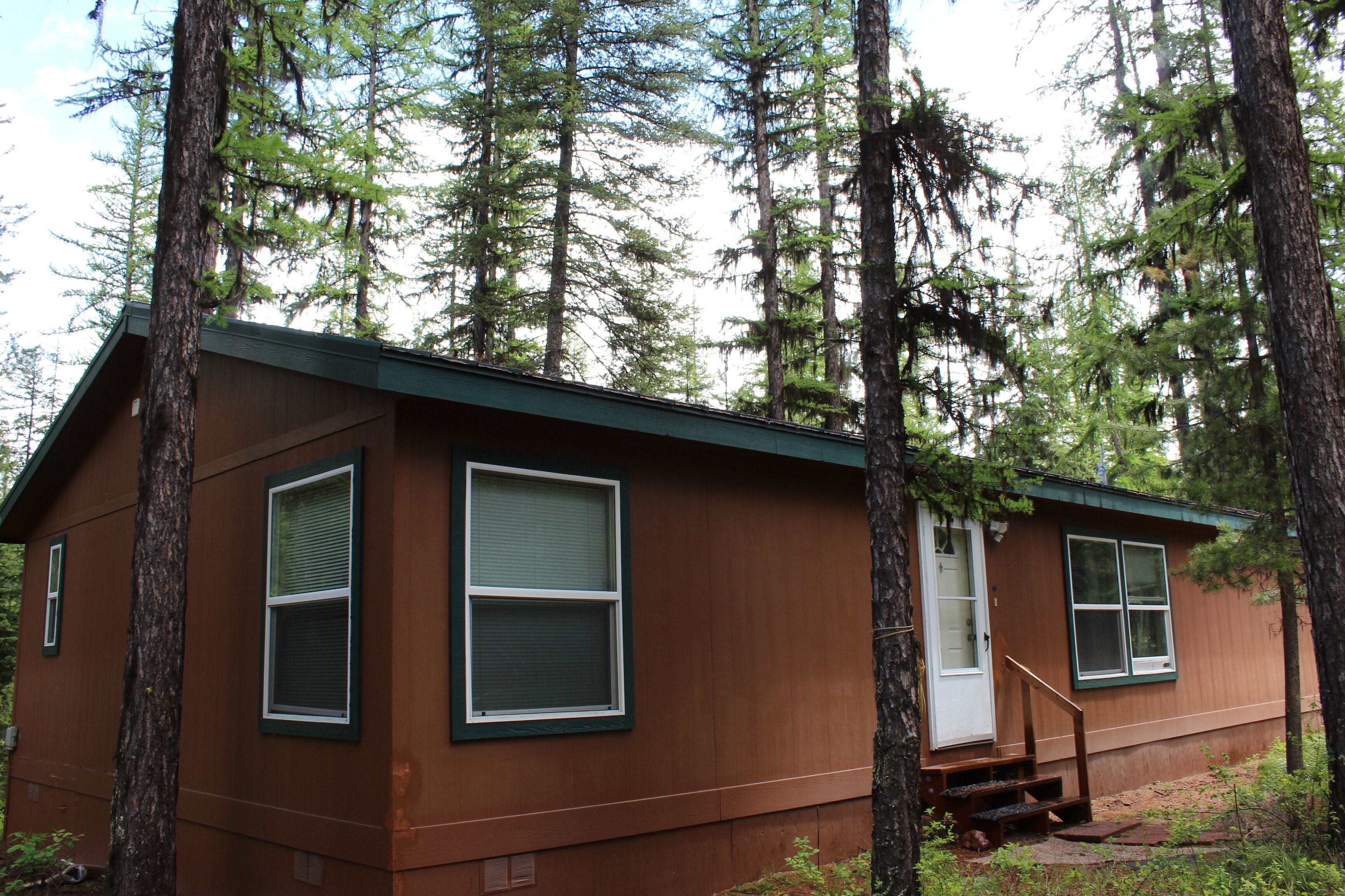 A cabin with a front door, two windows, and a staircase leading to a porch.
