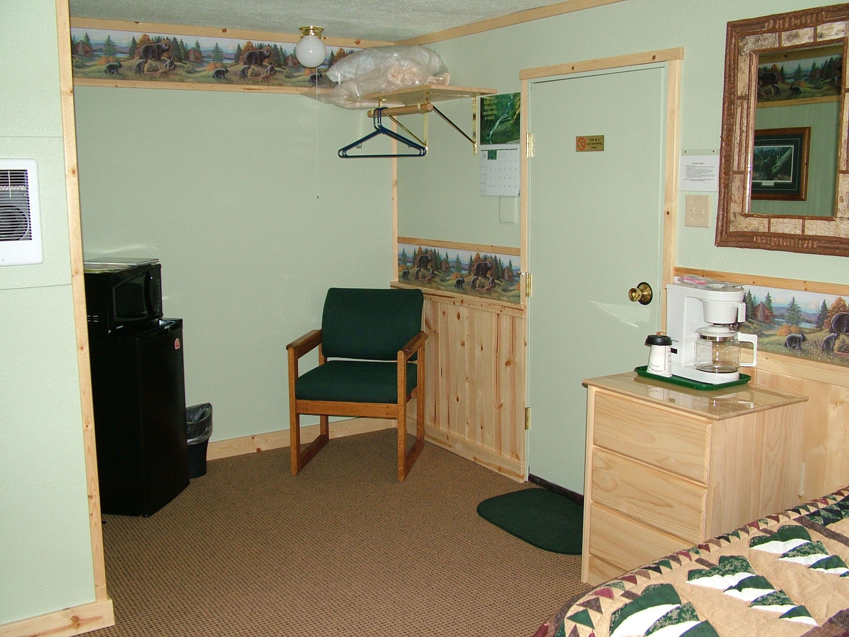 A small, compact room with a wooden chair, a small desk with a coffee maker, and a bed.
