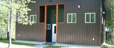 A modern, single-story building with a dark wooden exterior, a central door, and small windows.