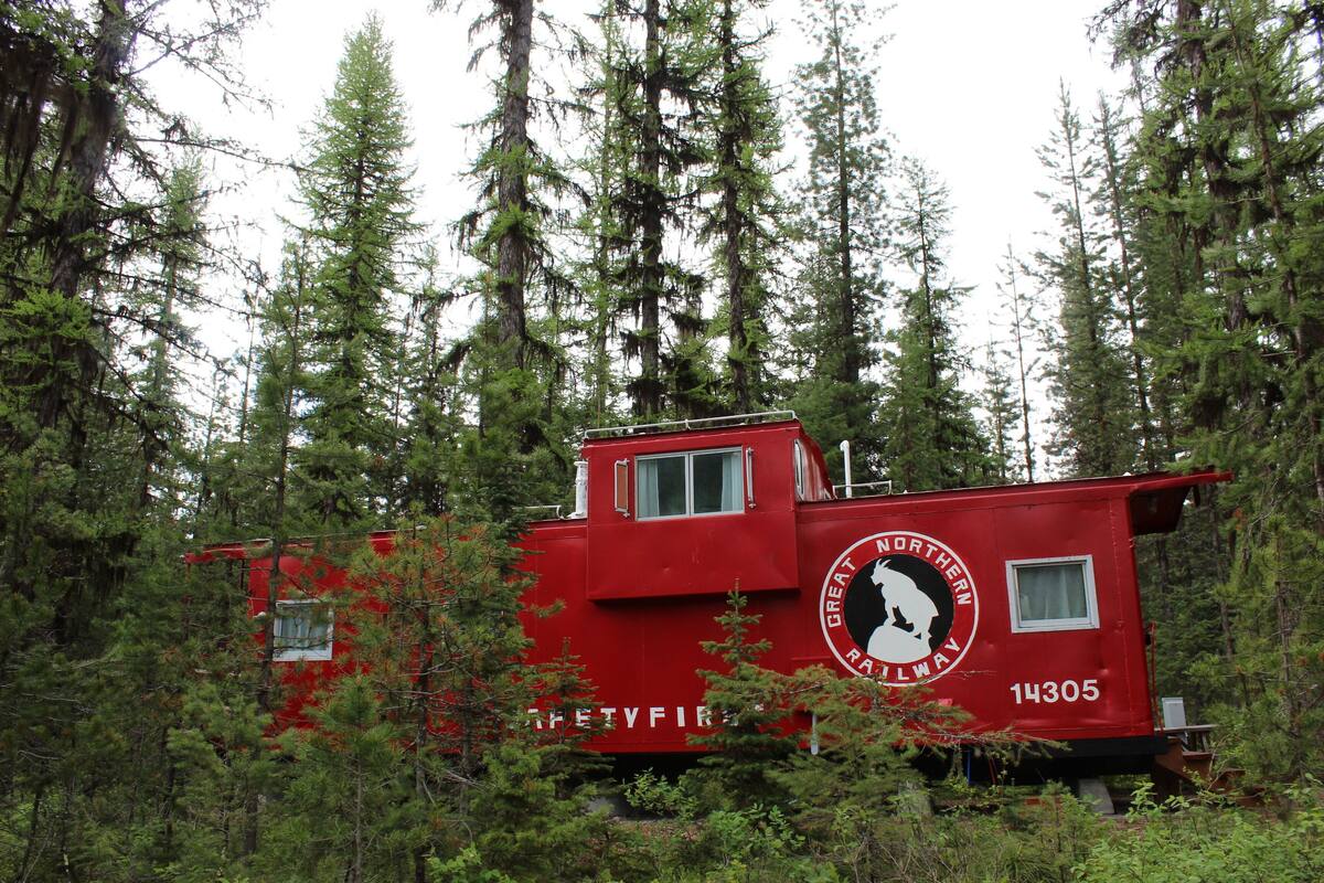 A red cabin with a Great Northern Railway logo, surrounded by dense forest.