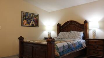 A bedroom with a wooden bed, two bedside tables with lamps, a wall-mounted painting, and a carpeted floor.