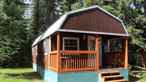 A small wooden cabin with a porch, a set of stairs leading to the entrance, and a surrounding natural environment. - Glacier Haven Inn (Essex)