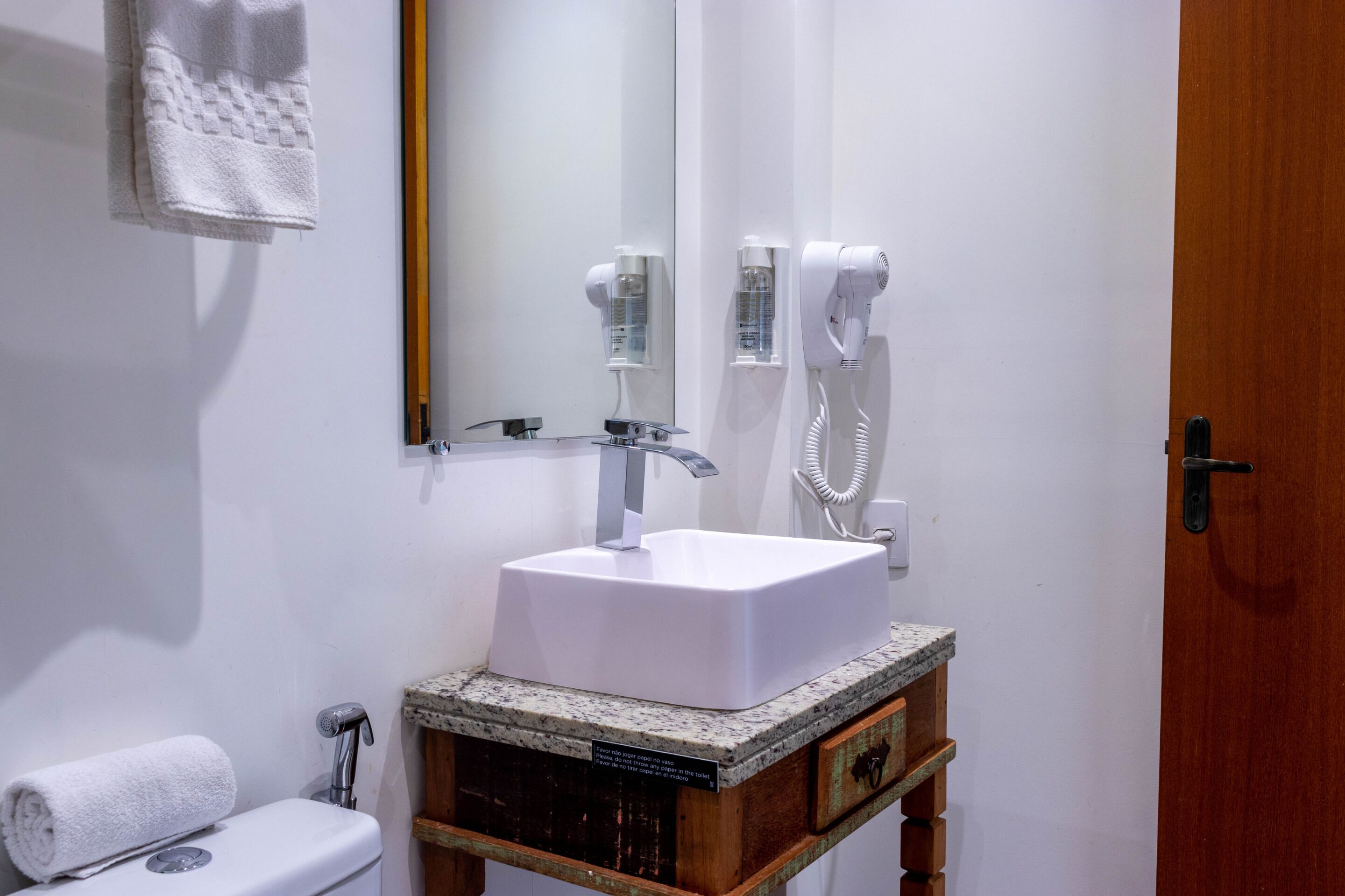 A bathroom with a white sink, a mirror, a hairdryer, and a towel hanging on the wall.