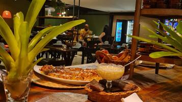 A restaurant interior with tables, chairs, a pizza, a dessert, and a beverage.