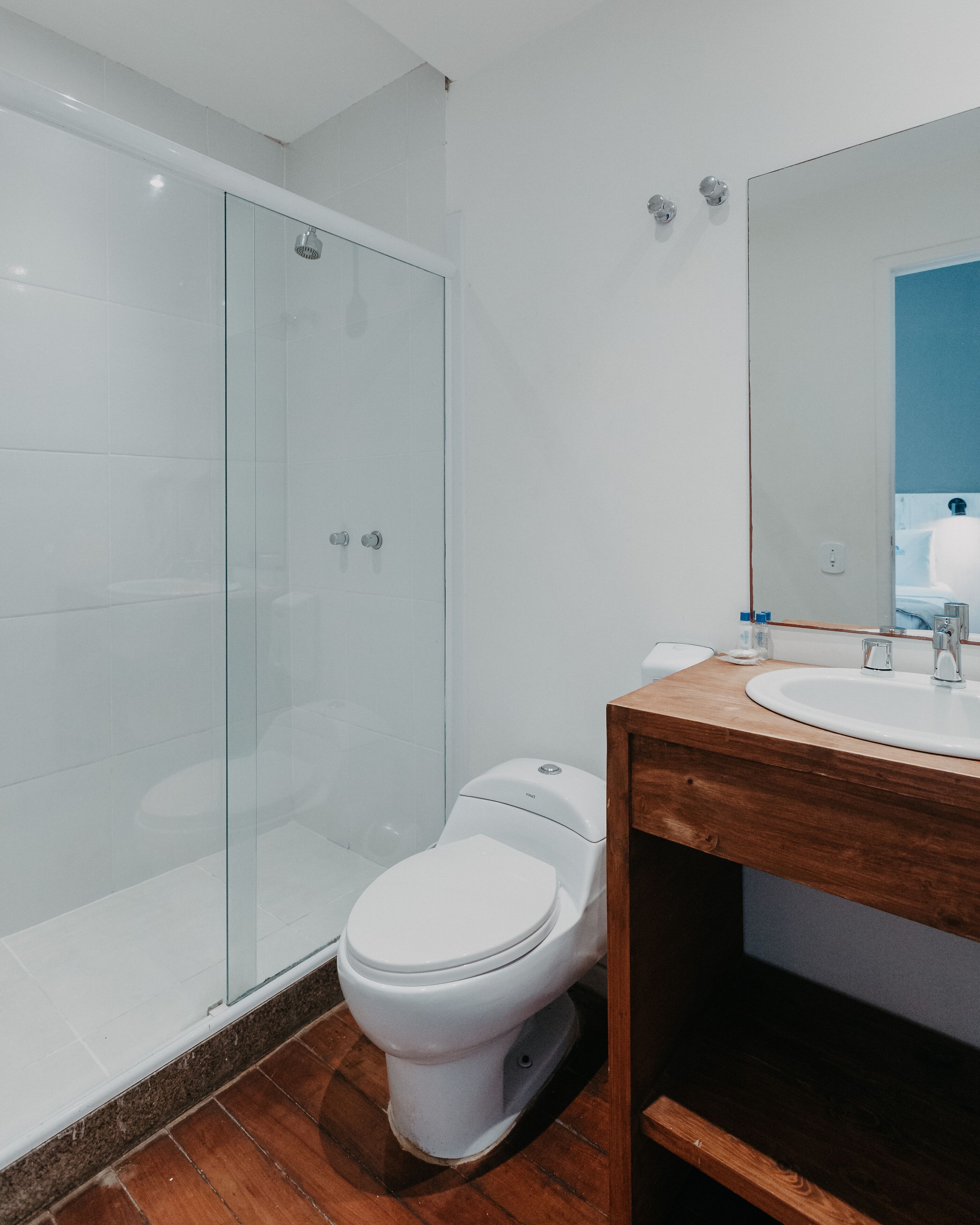Un baño moderno con cabina de ducha de vidrio, inodoro blanco y tocador de madera con lavamanos.