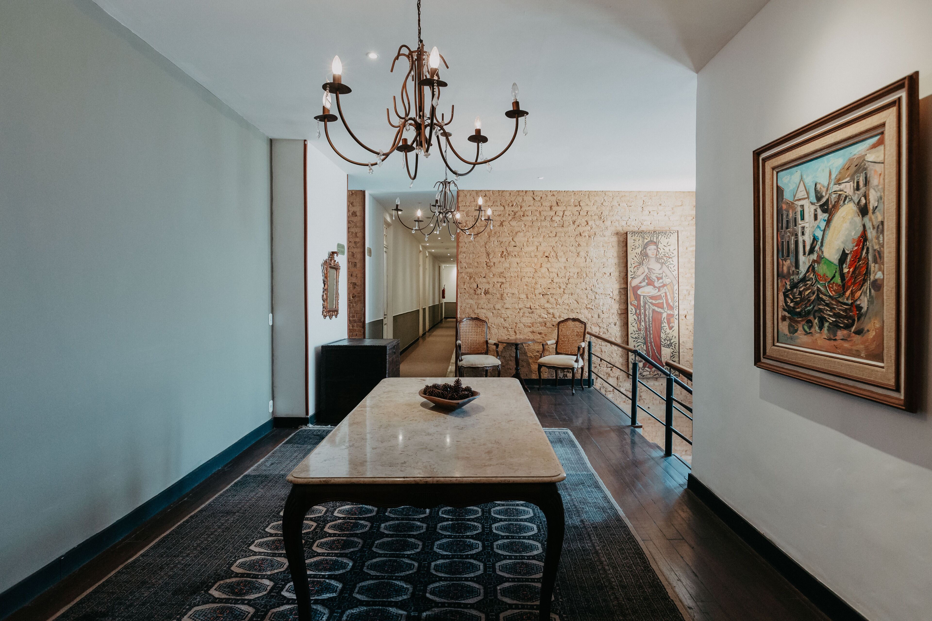 A hallway with a chandelier, a painting, and a staircase leading to another room.