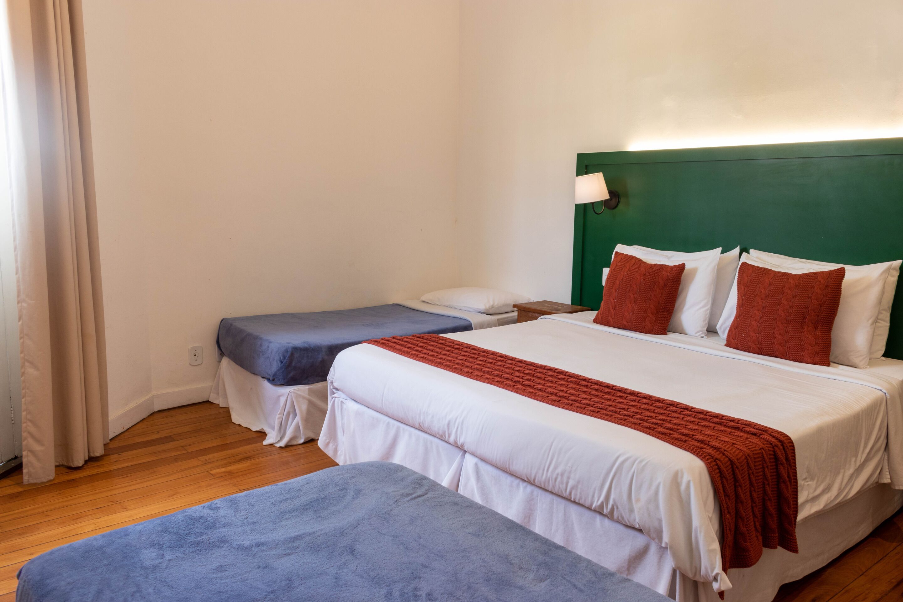 A hotel room with two beds, a green headboard, white bedding, and a red throw blanket.