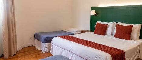 A hotel room with two beds, a green headboard, white bedding, and a red throw blanket.