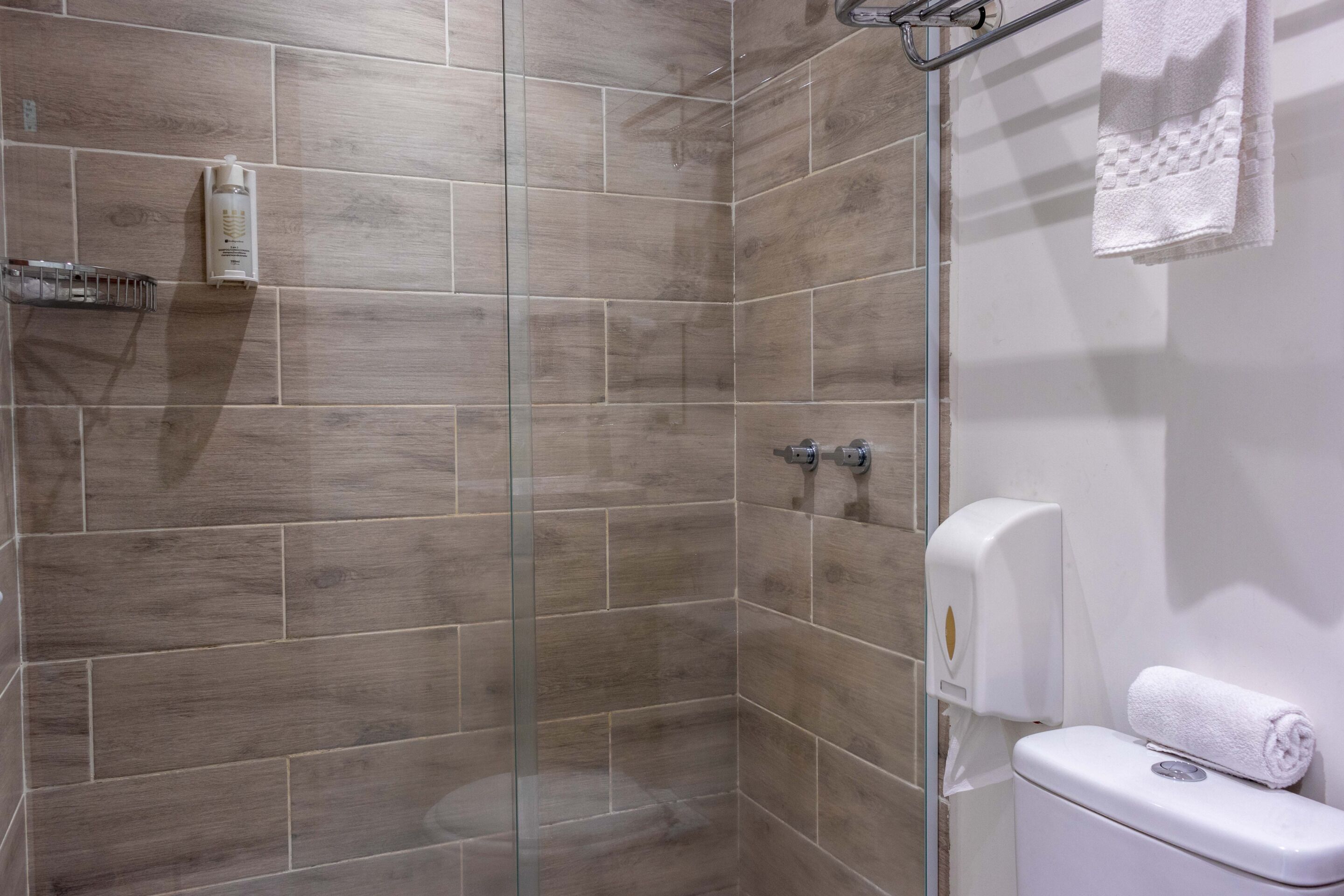 A modern bathroom with a glass shower enclosure, a toilet, and a hand dryer.
