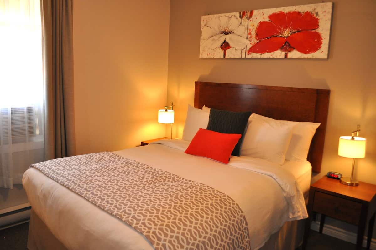 Une chambre d’hôtel avec un grand lit, deux lampes de chevet, une fen être avec des rideaux et une œuvre d’art florale accrochée au mur.
