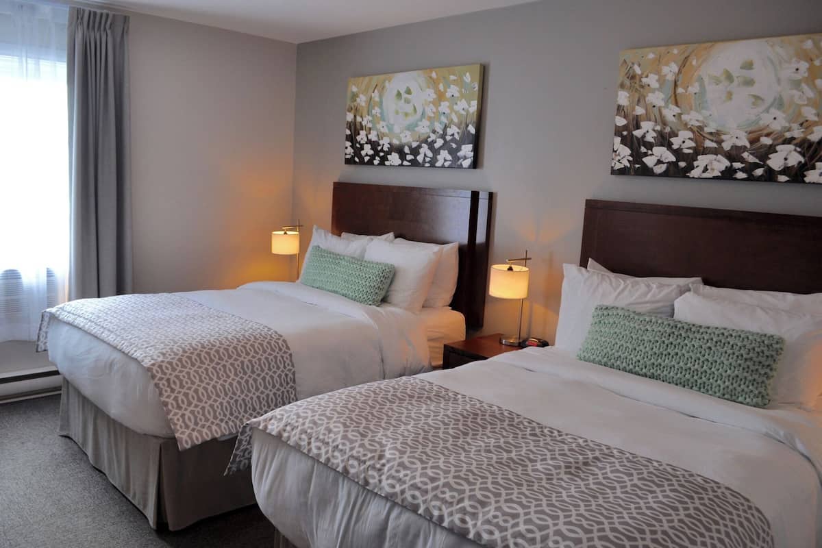 Une chambre d’hôtel avec deux lits, chacun doté d’une tête de lit, de lampes de chevet et de coussins décoratifs.