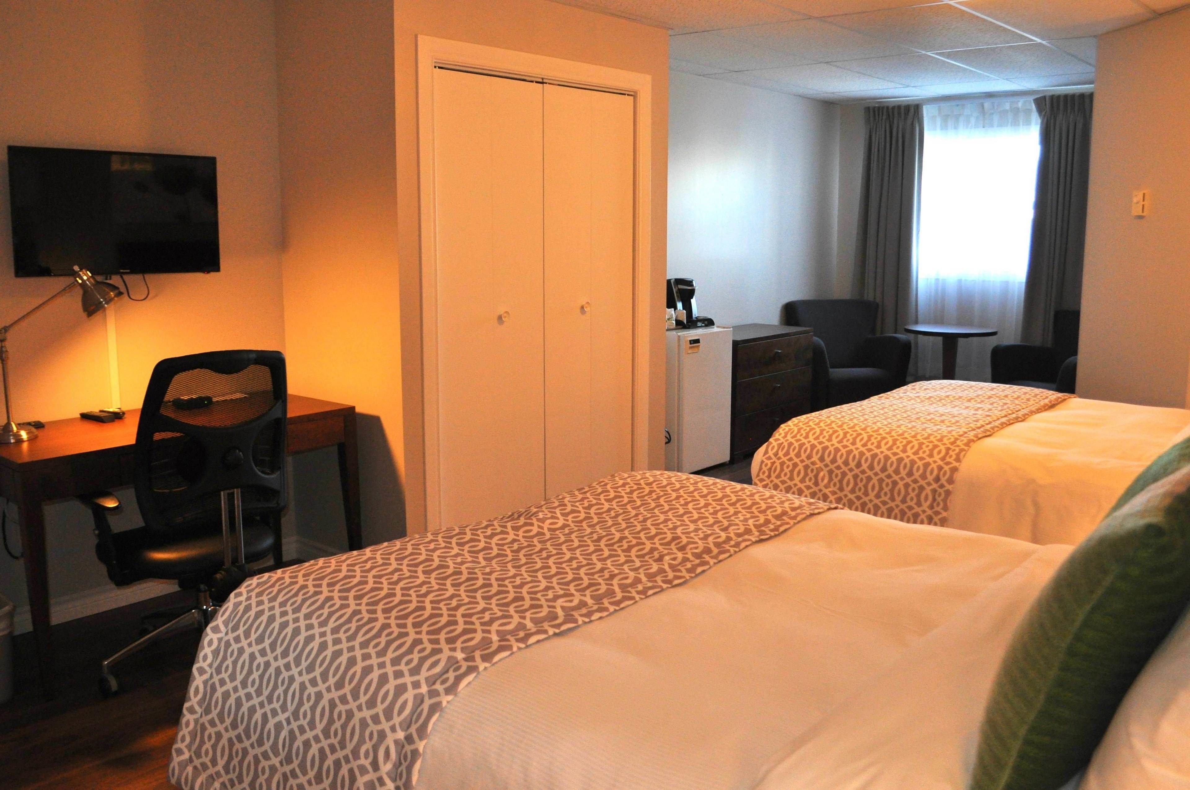 Ein Hotelzimmer mit zwei Betten, einem Schreibtisch mit Stuhl, einem Fernseher und einem kleinen Tisch.