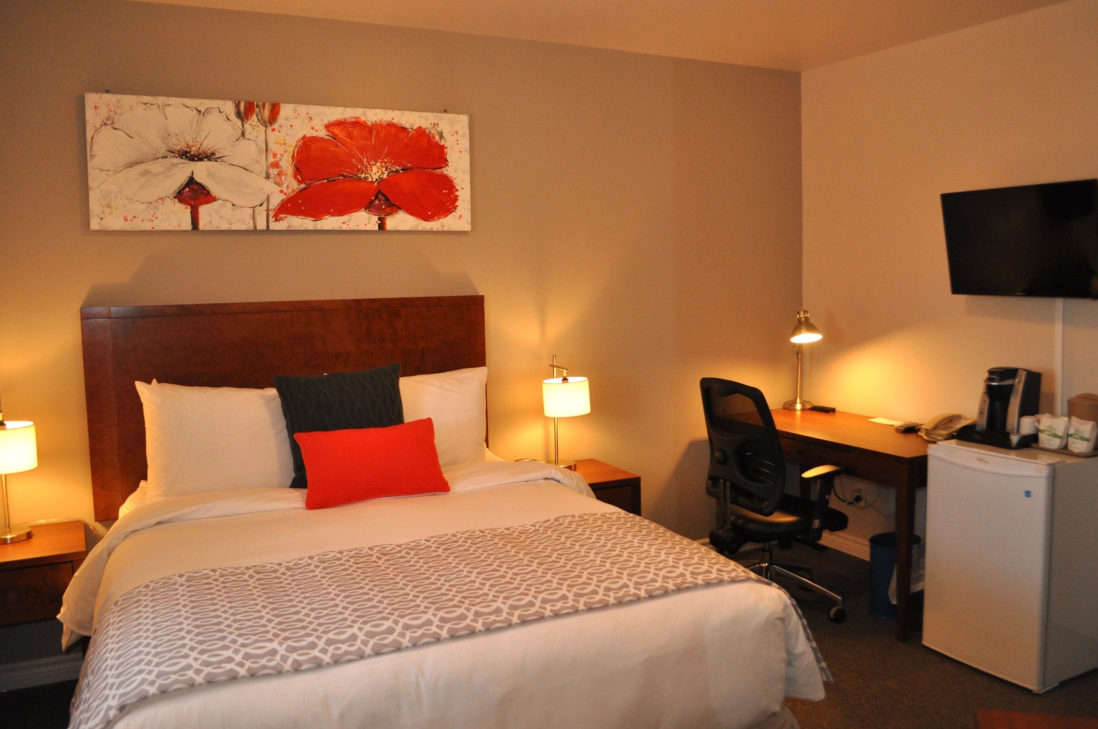 Une chambre d’hôtel avec un grand lit, un bureau, une chaise, une télévision et un réfrigérateur.