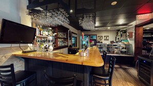 A bar area with a wooden counter, bar stools, a television, and a variety of bottles and glasses. - Auberge du Marchand (Maria)
