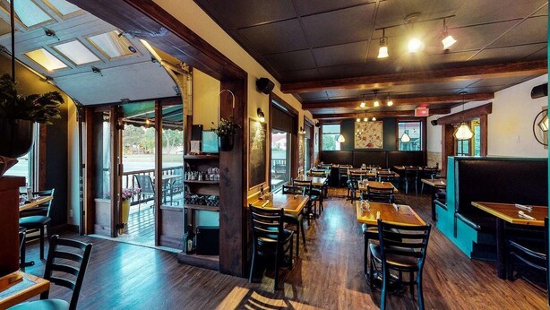 A restaurant interior with wooden tables and chairs, a bar area, and large windows offering views. - Auberge du Marchand (Maria)
