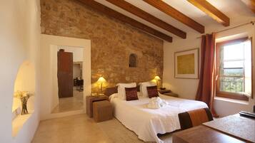 Un dormitorio con pared de piedra, vigas de madera, una cama con ropa de cama blanca, dos lámparas de noche y una ventana con cortinas.