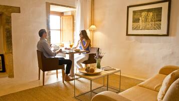 Una habitación con una mesa de comedor, dos sillas, un sofá, una mesita de centro y una obra de arte enmarcada en la pared.