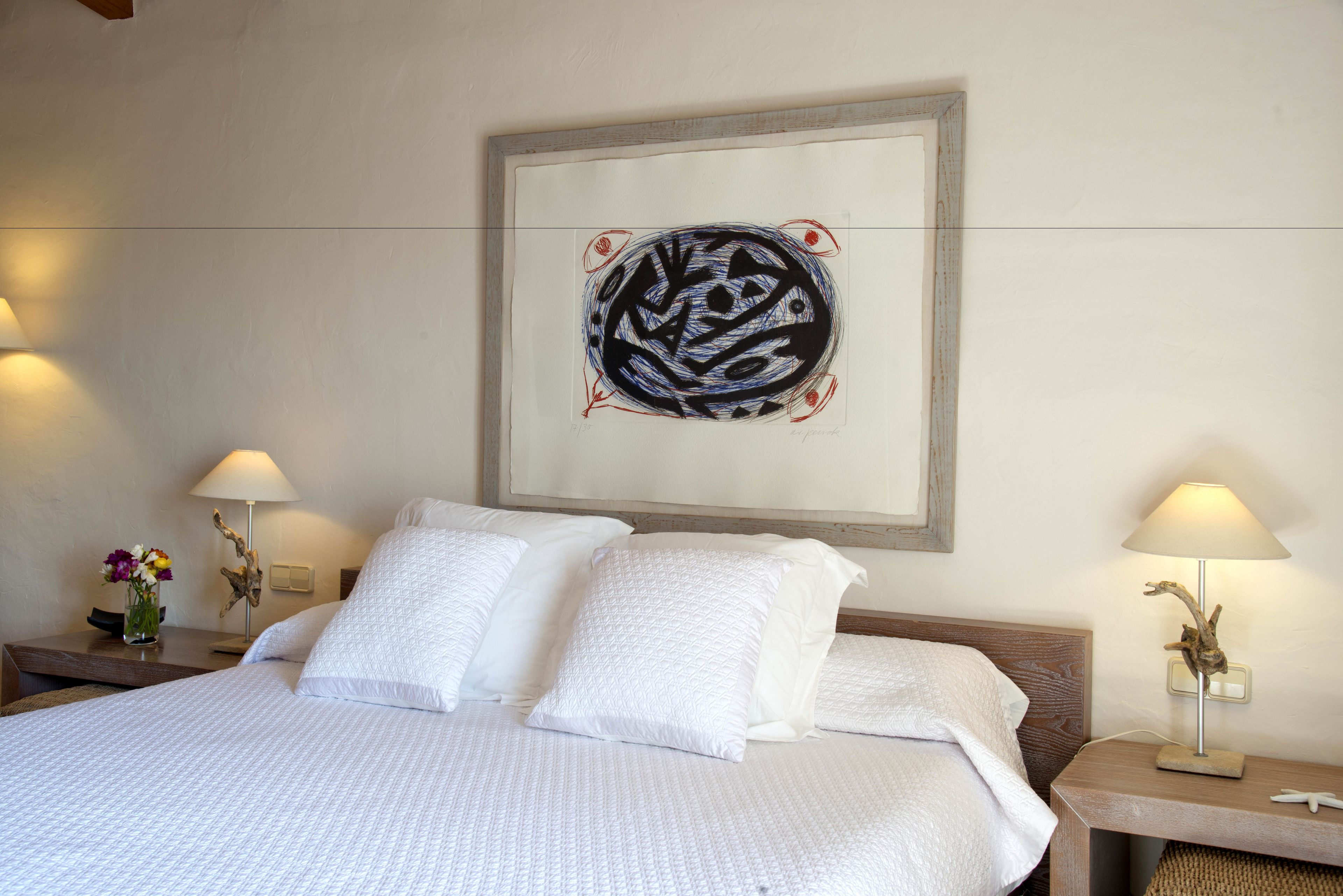 Una cama bien hecha con sábanas blancas, una obra de arte en la pared y dos lámparas de noche.