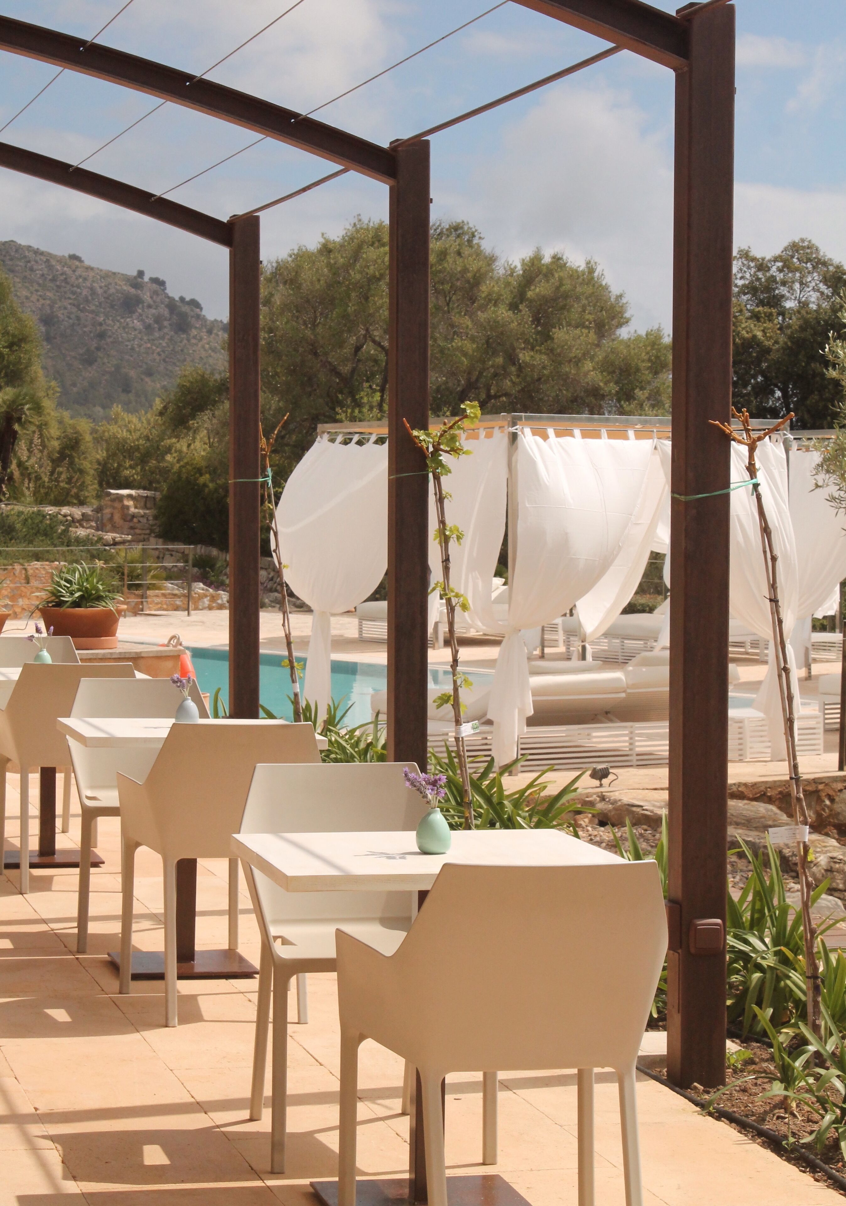 An outdoor patio with white tables and chairs, a pool, and a mountainous backdrop.