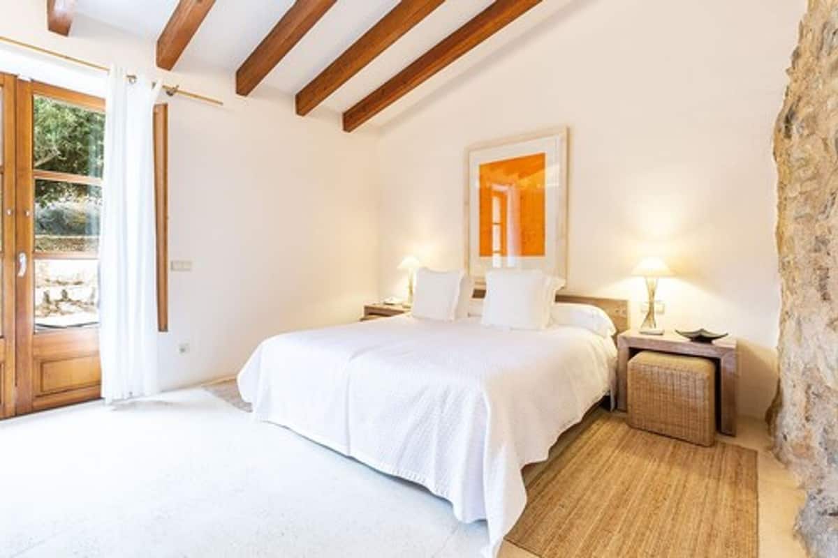 Un dormitorio con cama, mesitas de noche, un espejo y una pared de piedra.