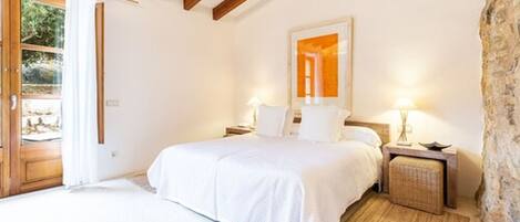 A bedroom with a bed, bedside tables, a mirror, and a stone wall.
