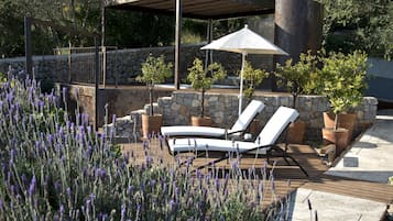 Una terraza de madera con dos sillones de descanso y una pérgola con sombrilla.