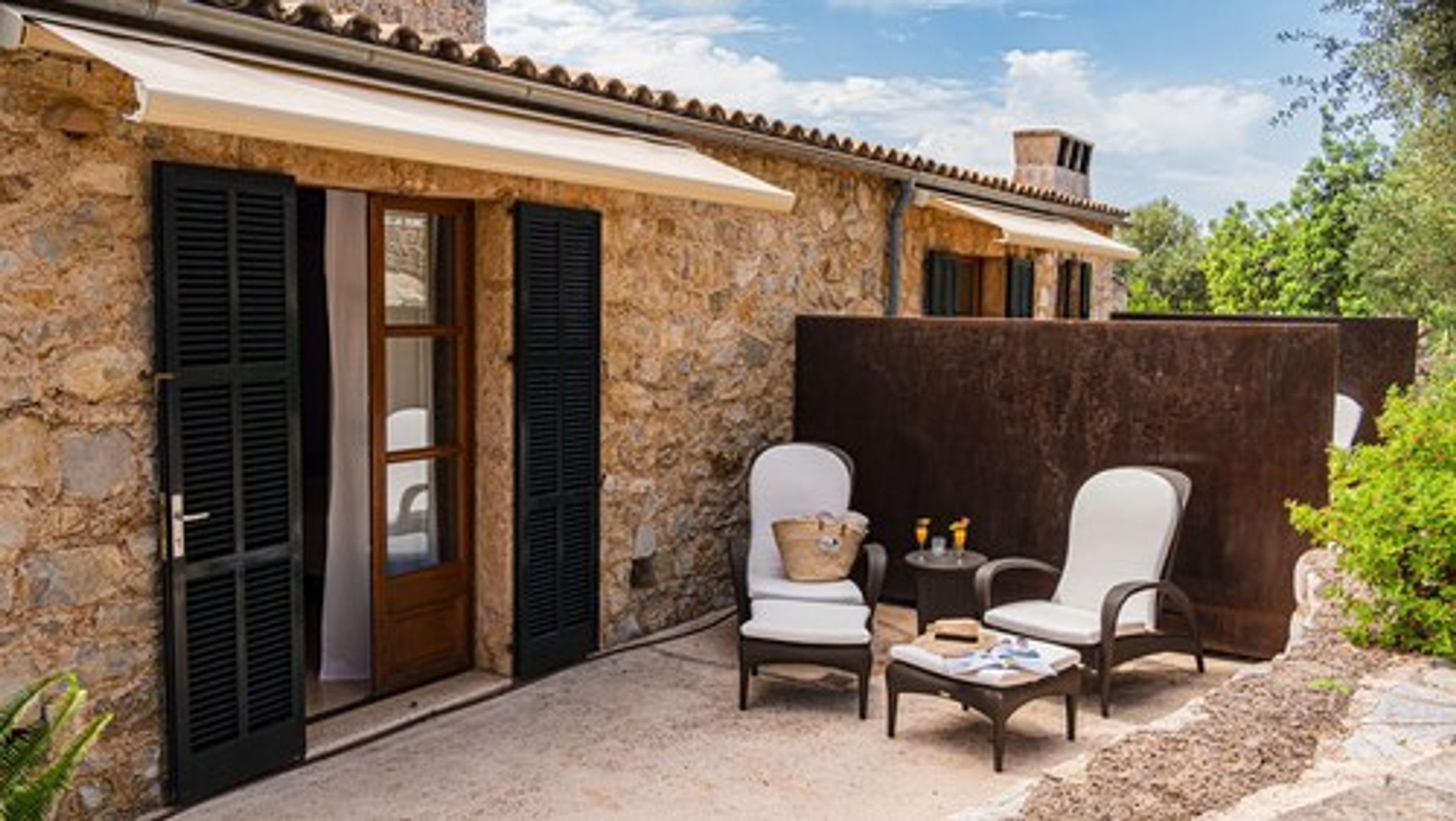 A stone building with a covered patio, two white chairs, a small table, and a basket.