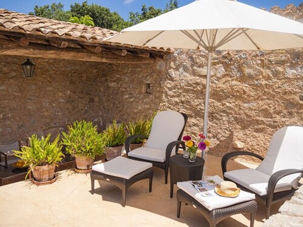 An outdoor patio with wicker furniture, potted plants, and a large umbrella.
