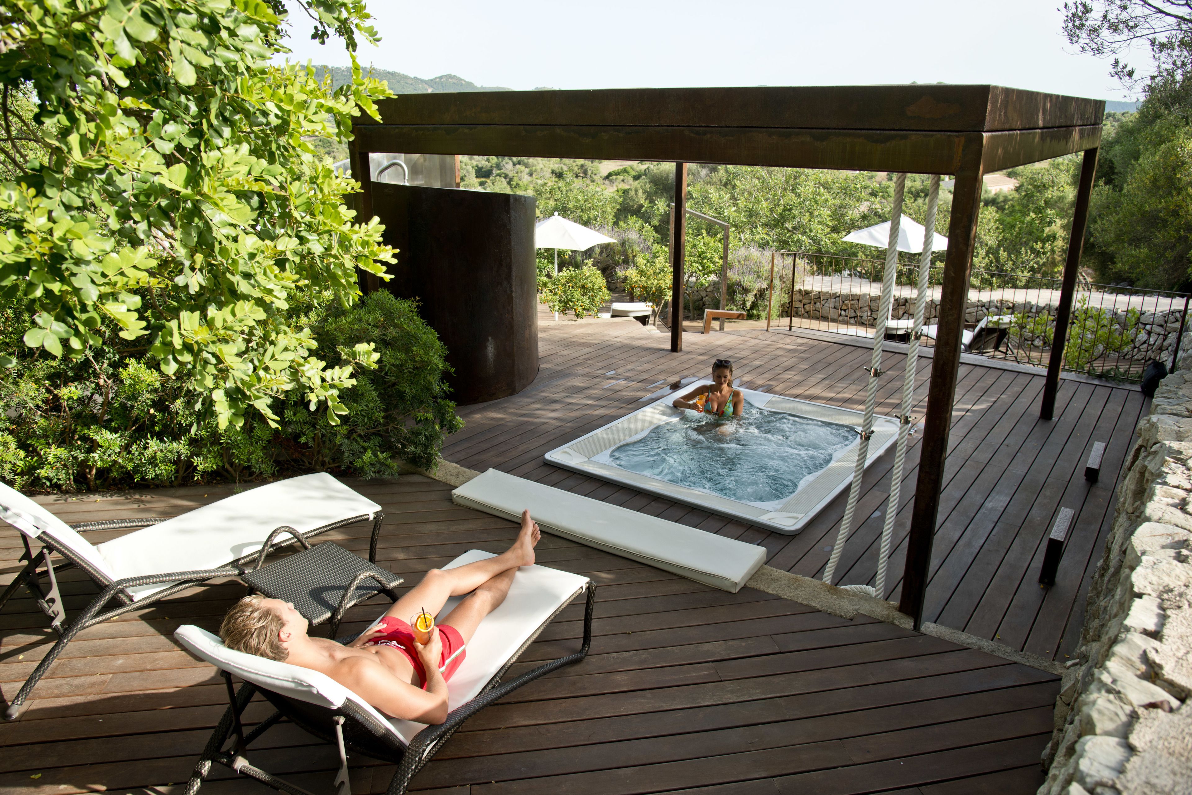 A wooden deck with lounge chairs, a hot tub, and a pergola providing shade.