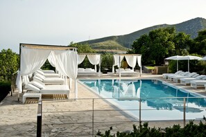 Ein Poolbereich mit weißen Sonnensegeln, Liegestühlen und freiem Blick auf die Berge.