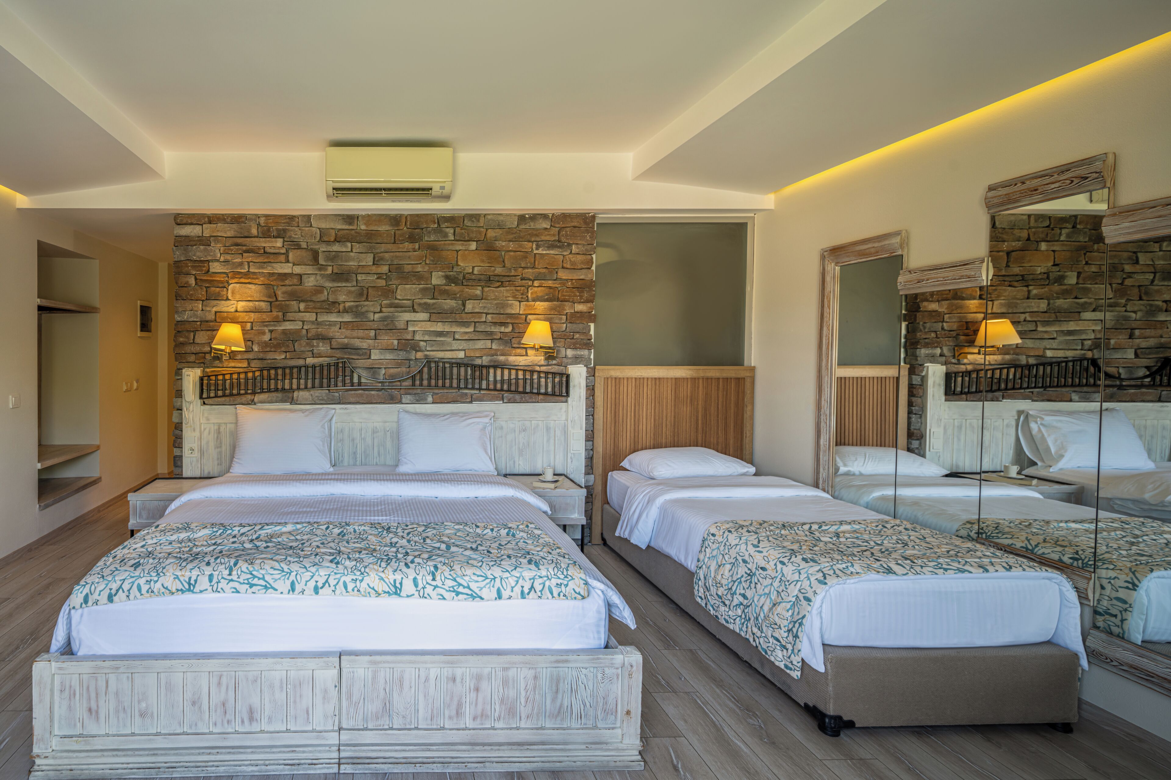 A hotel room with a stone wall, two beds, a mirror, and a wooden floor.