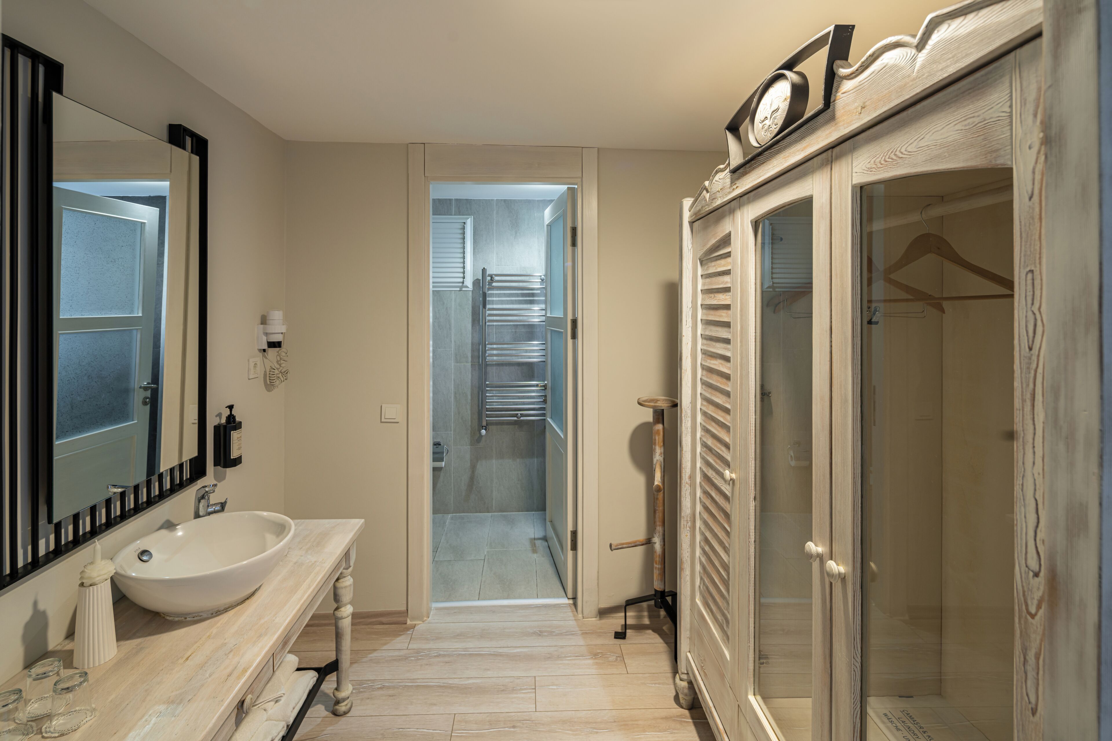 A bathroom with a large sink, mirror, and a walk-in closet with a hanging rod.