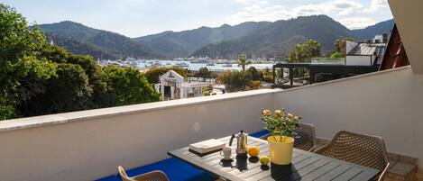 Un balcon avec une table, des chaises et une vue sur la mer et les montagnes.