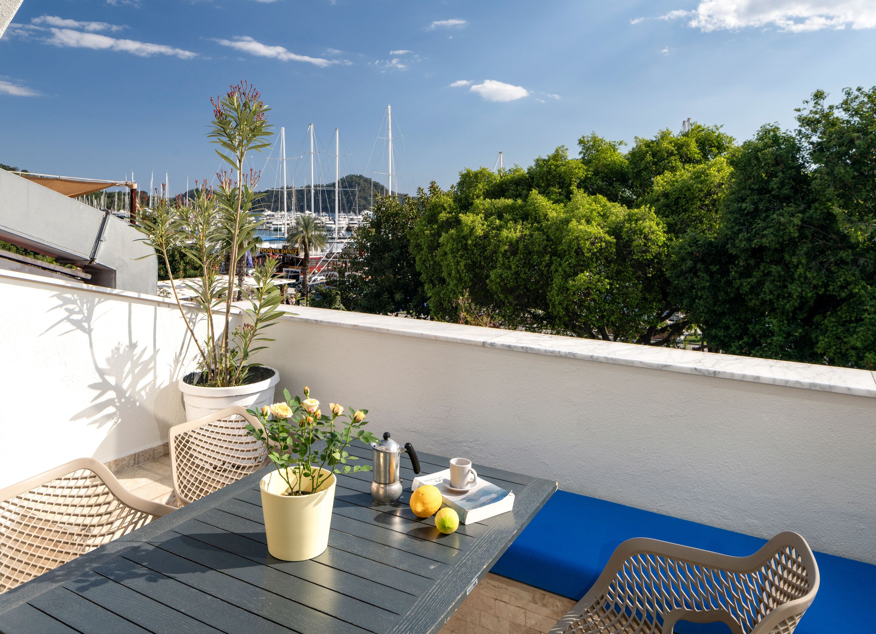 A balcony with a table, chairs, a potted plant, a coffee pot, and lemons.