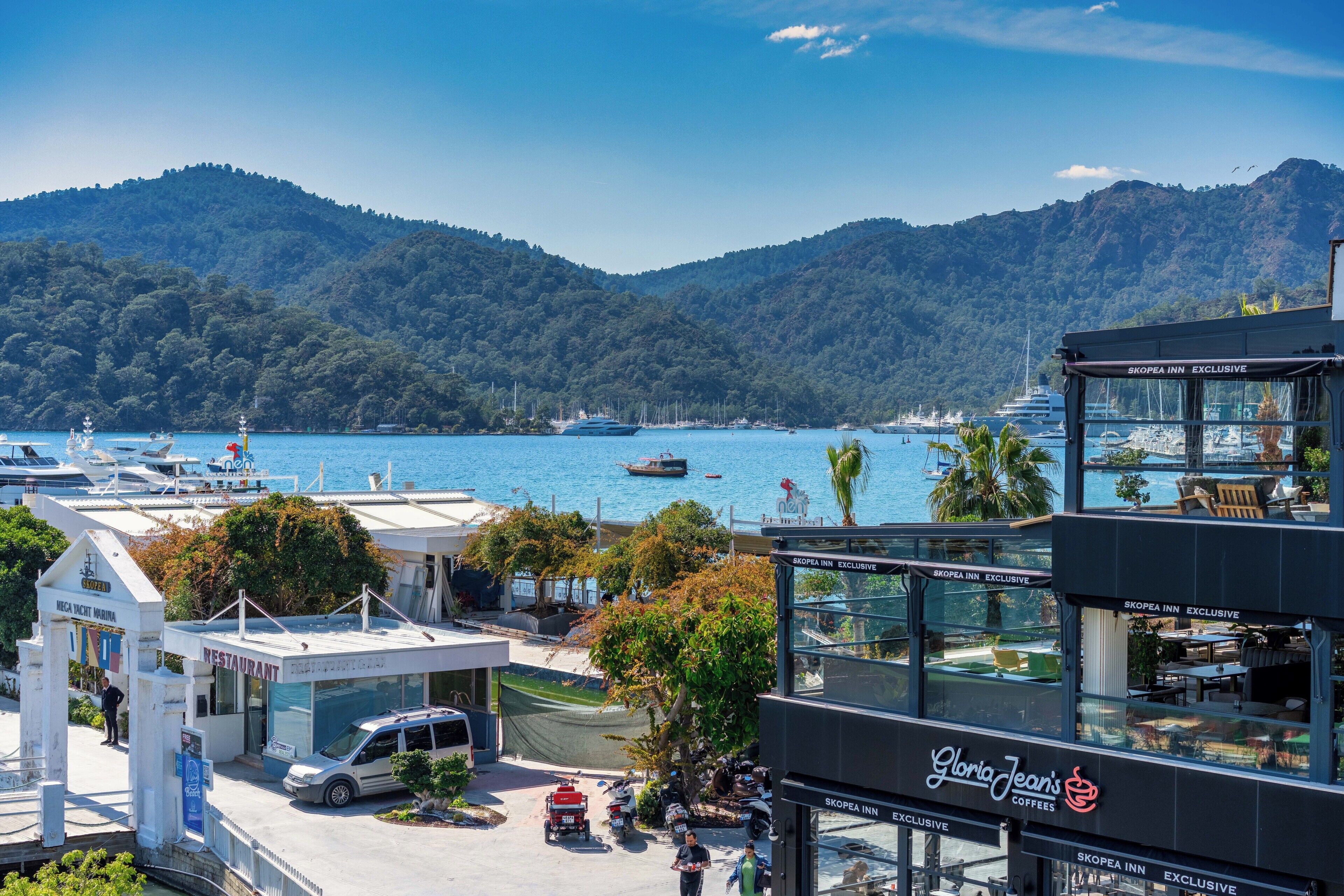 A marina with boats, a restaurant, and a coffee shop with a view of the water and mountains.