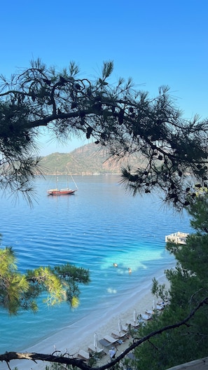 A beach with clear water, a boat, and a distant mountain. - Dedeminn Marina Hotel (Fethiye)