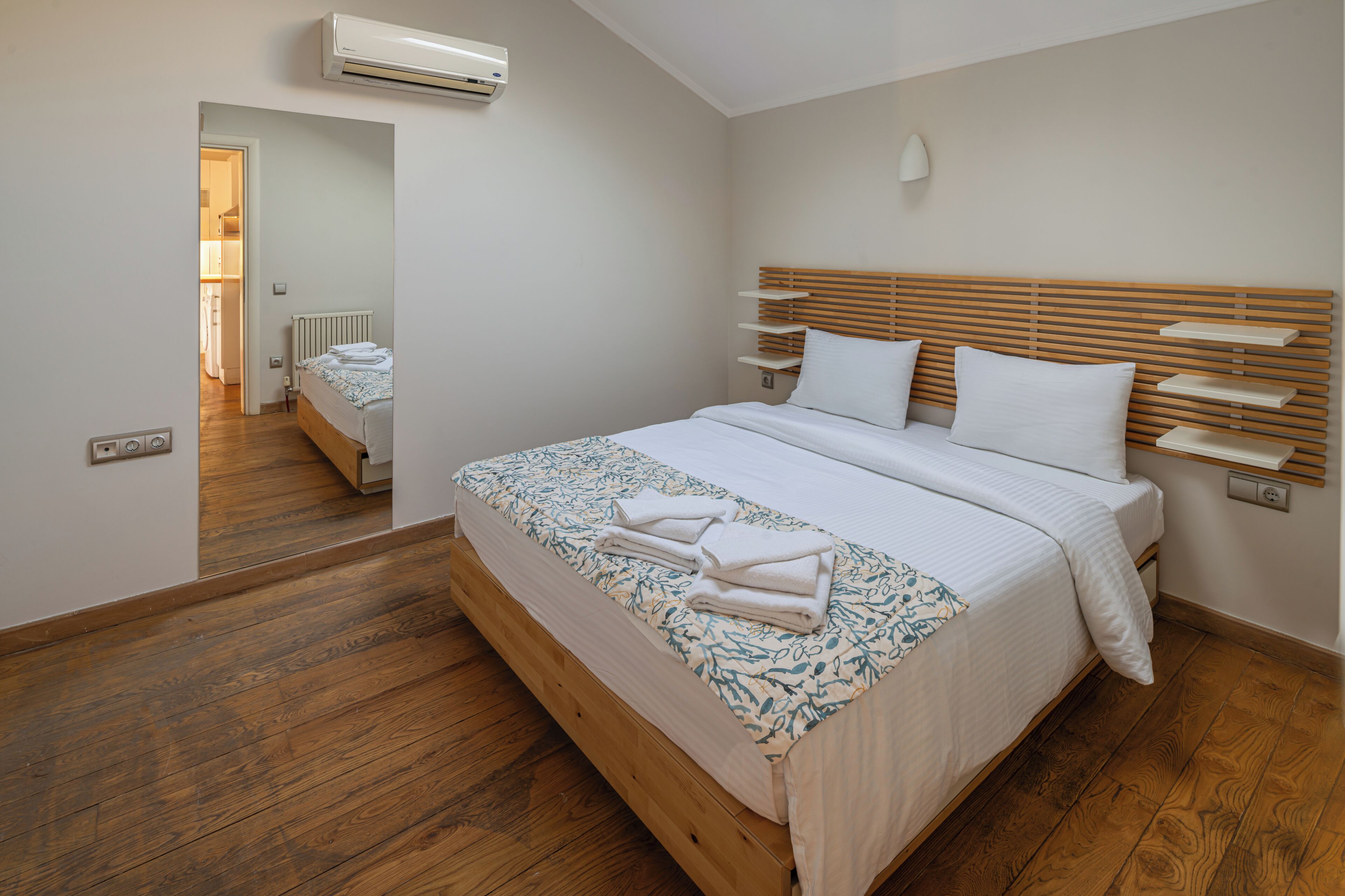 A bedroom with a wooden bed, white bedding, a bedside lamp, and a view of a bathroom.