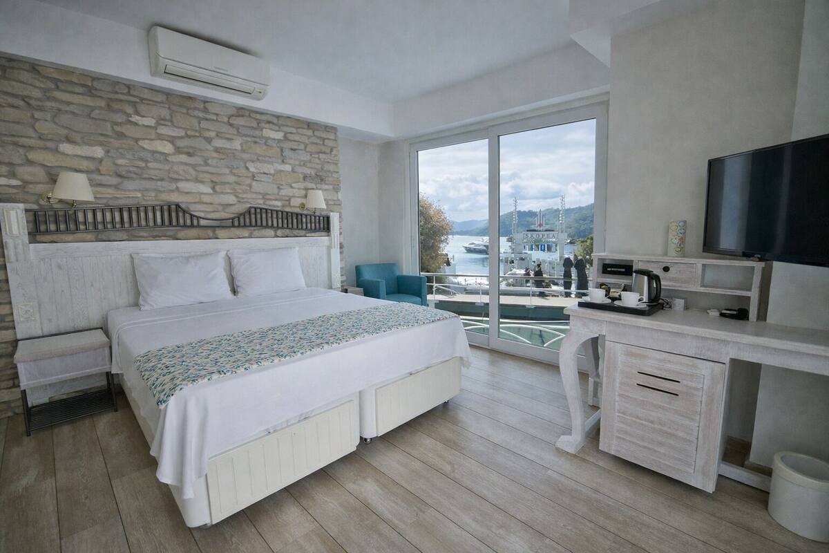A bedroom with a bed, a desk, a TV, and a view of a harbor.