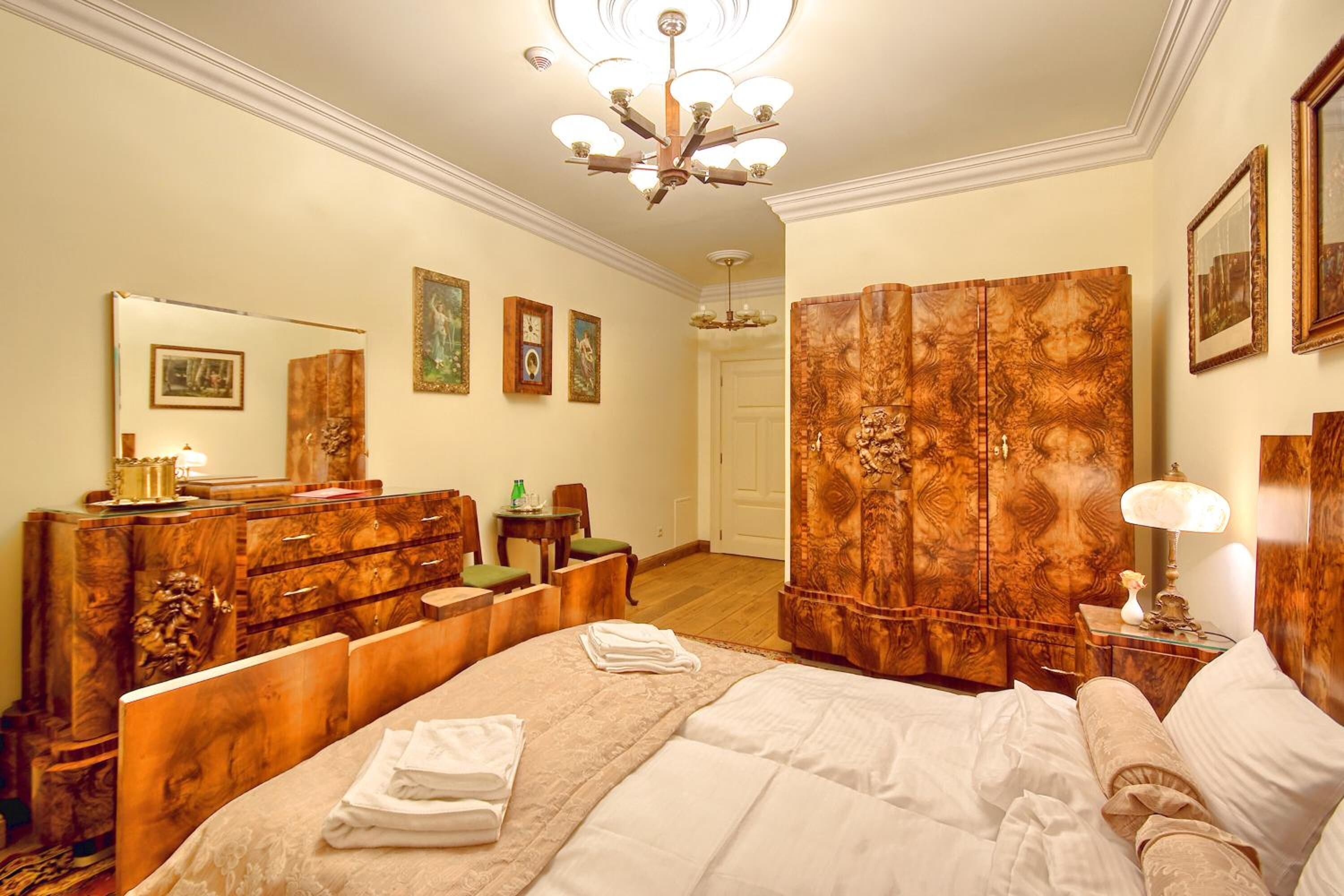 Habitación de hotel con una cama grande, muebles de madera, un candelabro y cuadros enmarcados en las paredes.