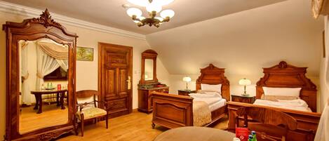 Una habitación de hotel con un espejo grande, dos camas, una mesa de comedor con sillas y una araña.