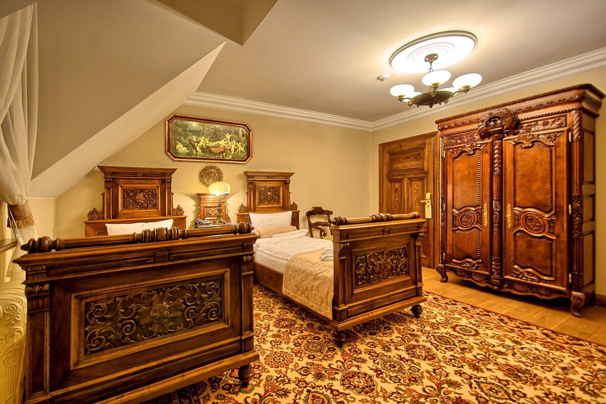 Um quarto tradicional com uma cama grande, móveis de madeira ornamentados, um candelabro e um tapete estampado.