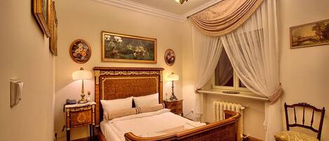 A traditional bedroom with a wooden bed, two bedside tables, a chandelier, and a window with curtains.